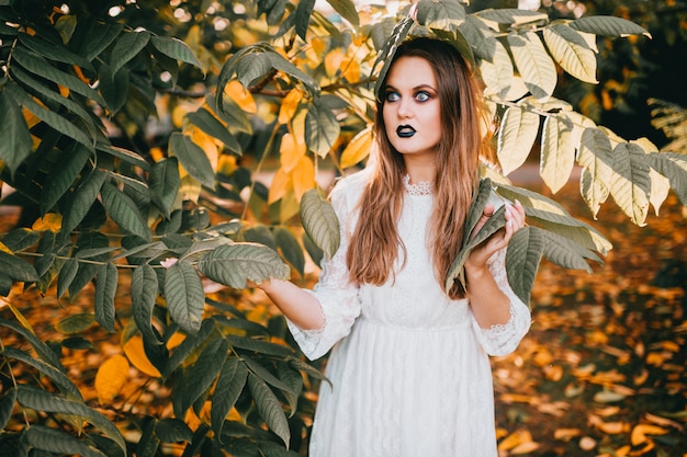 Menina bonita com maquiagem gótica e expressão de rosto engraçado, posando no parque de verão.