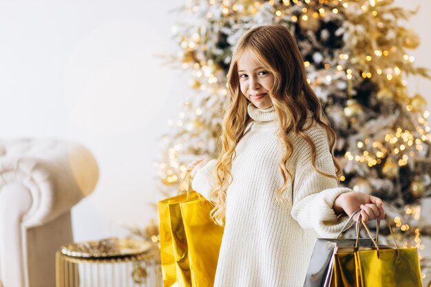 Menina bonita com presentes de Natal sorrindo e de pé perto da árvore de Natal