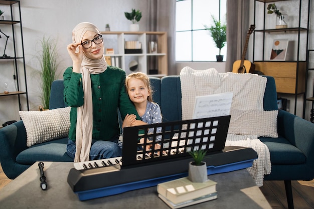 Menina bonita com professor muçulmano de música tendo aula de piano na escola de música