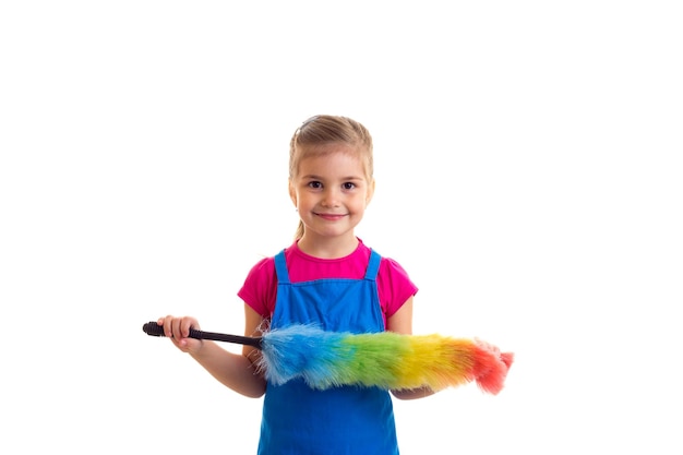 Menina bonita com rabo de cavalo longo vestindo camisa rosa e avental azul com espanador colorido