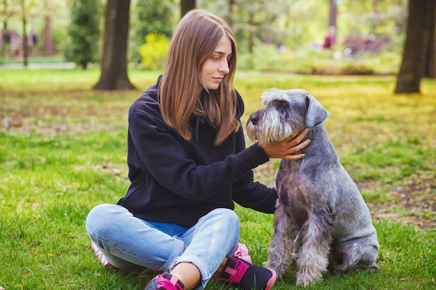 Menina bonita com seu cachorro schnauzer no parque natural ao ar livre está de pé e posando