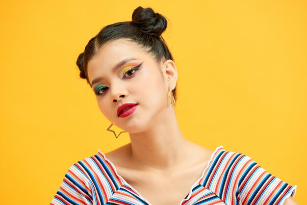 Menina bonita com sorrisos fofos de pãezinhos. Mulher com sombras coloridas em um fundo amarelo