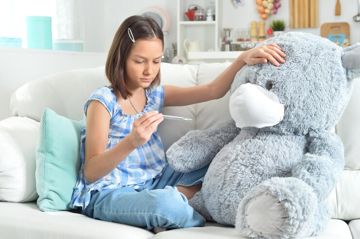 Foto menina bonita com termômetro brincando com um ursinho de pelúcia de brinquedo em máscara facial
