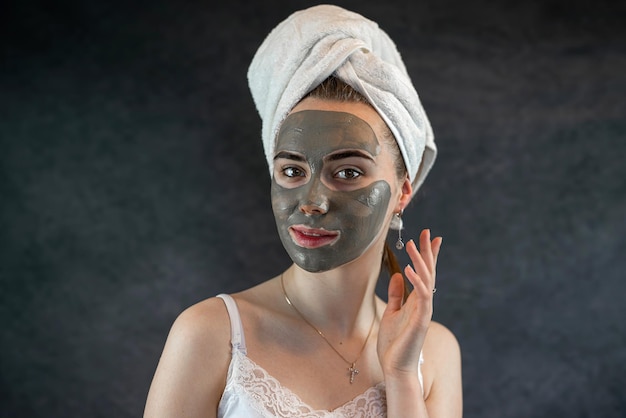 Menina bonita com toalha branca com máscara facial de lama verde isolada em preto