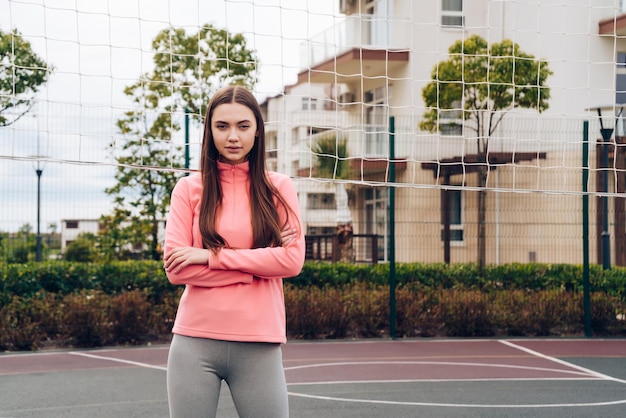 Menina bonita com uma jaqueta rosa ganha força e energia antes do treino, no campo de esportes