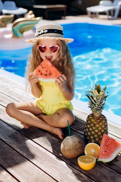 Menina bonita comendo melancia à beira da piscina