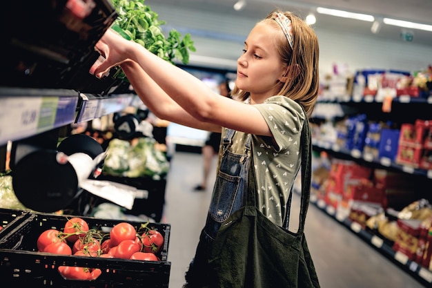 Menina bonita comprando tomates no supermercado menina bonita pré-adolescente escolhendo legumes em