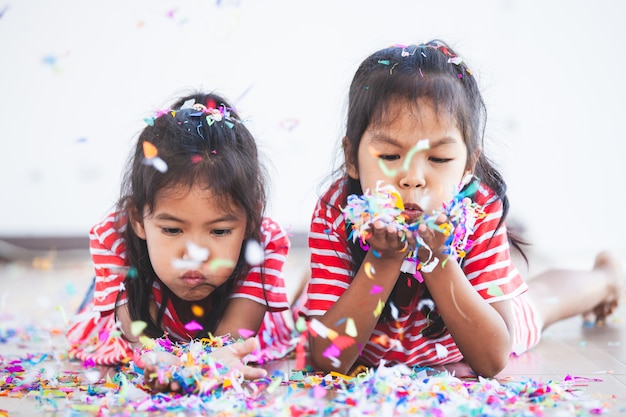 Menina bonita criança asiática e sua irmã brincar com confetes coloridos juntos para comemorar na festa