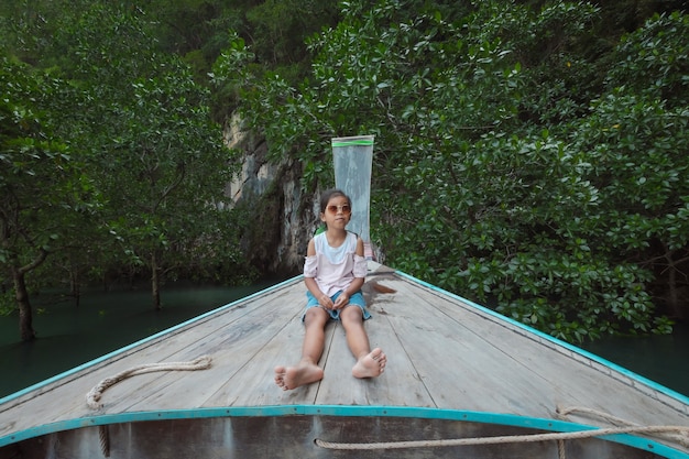 Menina bonita criança asiática sentada na cabeça do barco longtail de madeira.