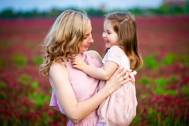 Menina bonita criança sorridente com a jovem mãe em família olhar no campo de flores de trevo em vez por do sol