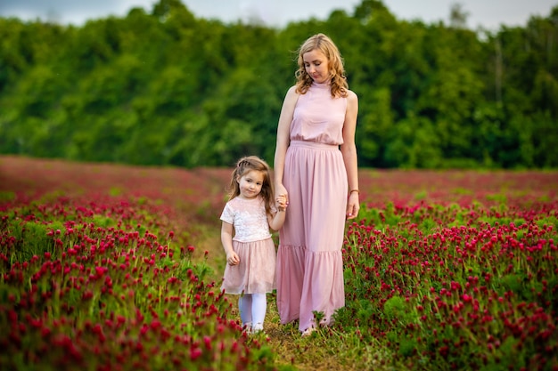 Menina bonita criança sorridente com a jovem mãe em família olhar no campo de flores de trevo em vez por do sol