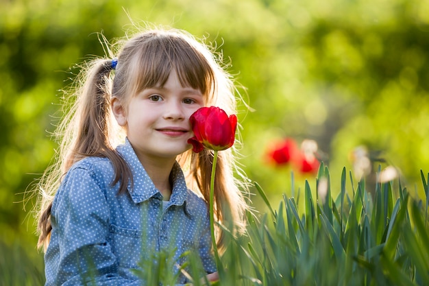 Menina bonita criança sorridente com olhos cinzentos e cabelos longos com flor tulipa vermelha brilhante. Amor ao conceito de natureza.