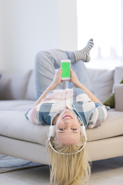 Foto menina bonita curtindo música através de fones de ouvido, deitada no sofá em casa