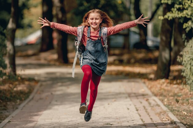 Menina bonita da escola com mochila correndo e rindo. Aluna engraçada garota feliz depois da aula de educação no parque de outono