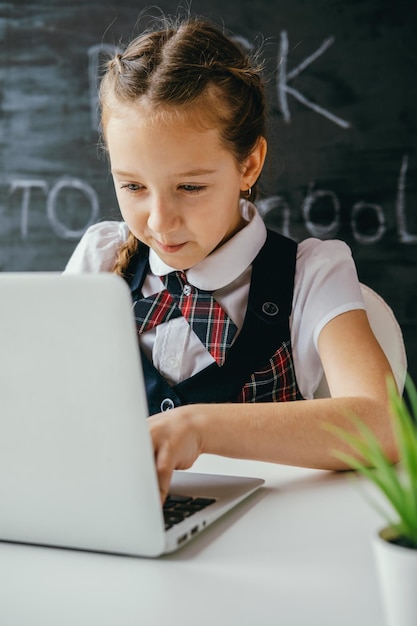 Menina bonita da escola sentada na mesa e usando o computador De volta à escola e ao conceito de aulas on-line