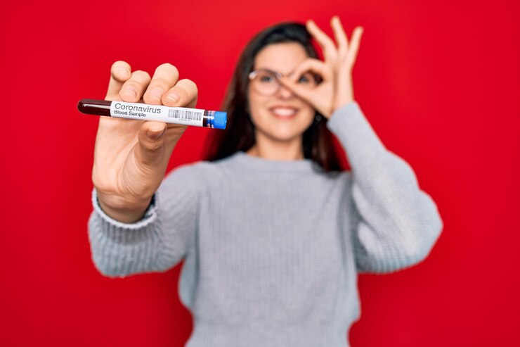 Foto menina bonita de óculos segurando amostra de sangue de laboratório da doença de coronavírus com cara feliz sorrindo fazendo sinal de ok com a mão no olho olhando por entre os dedos