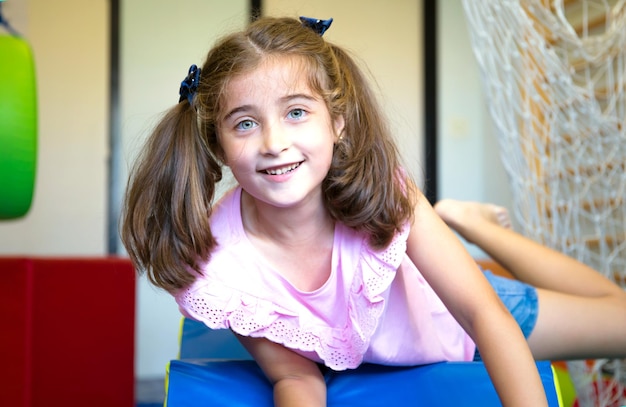 Menina bonita, de olhos claros, deitada em tapetes no ginásio da escola.