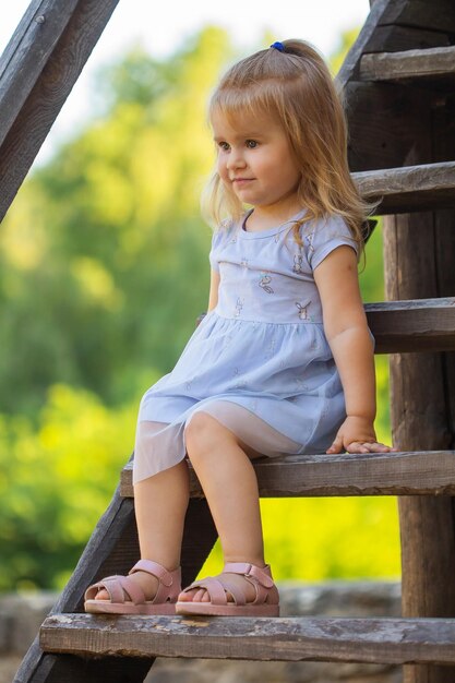 Foto menina bonita de vestido azul na escada de madeira no verão