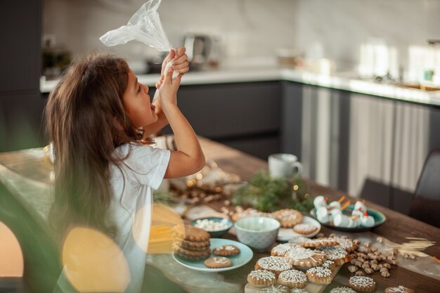 Foto menina bonita decora pão de gengibre com preparação de glacê de açúcar para o conceito de natal