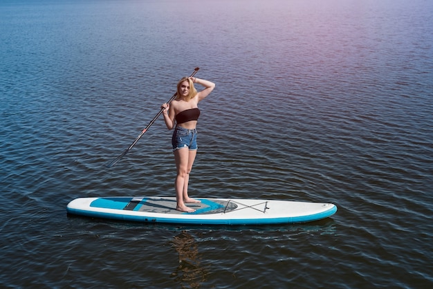 Menina bonita deitada na prancha de remo na água do lago azul escuro. Conceito de viagem ou férias