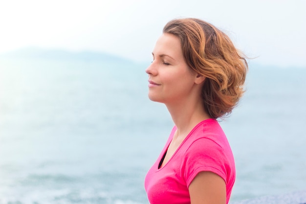 Menina bonita, desfrutando de andar no clima ensolarado de bom verão. Jovem mulher respirando profundamente, profundamente o ar do mar, sorrindo com os olhos fechados. A vida é boa. Senhora relaxada sonhando. Calma, conceito de meditação