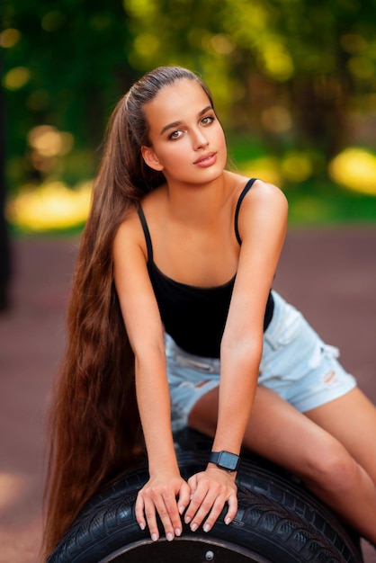 Foto menina bonita do esporte em shorts curtos azuis com cabelos longos no ginásio ao ar livre.