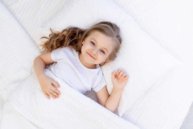 Menina bonita dormindo em uma cama em um travesseiro de algodão branco sob um cobertor bebê saudável dormir à noite