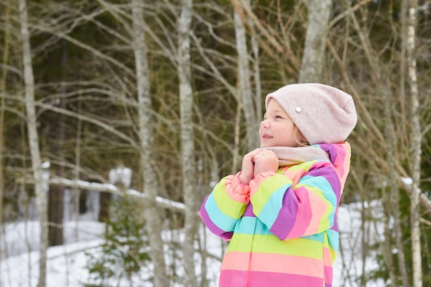 Menina bonita e alegre em uma floresta de neve brilhante sol de primavera neve