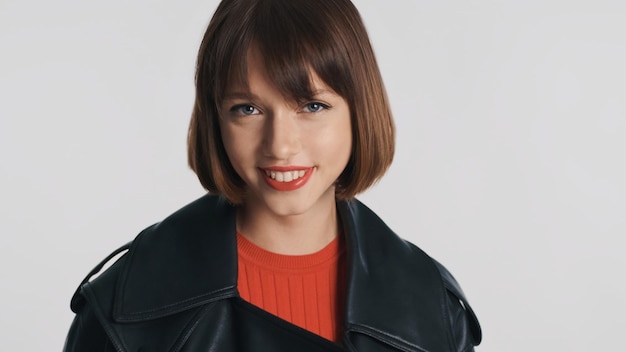 Foto menina bonita e bonita com cabelo bob olhando alegremente na câmera e sorrindo sobre fundo branco. expressão positiva