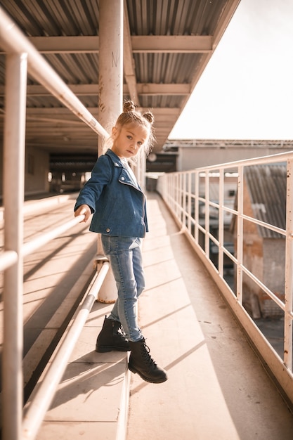 Menina bonita e elegante de cerca de sete anos com uma jaqueta jeans andando na rua