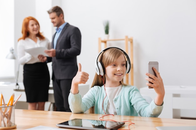 Menina bonita e sociável usando seu smartphone para fazer uma foto e compartilhá-la com os amigos online