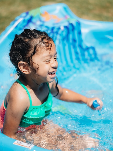 Menina bonita e sorridente sentada na piscina ao ar livre