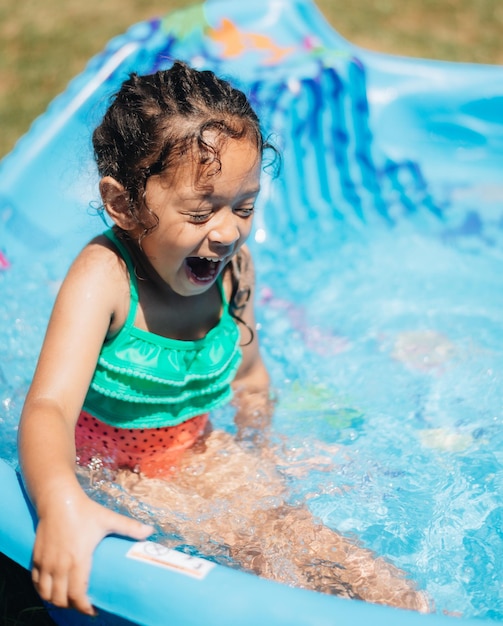 Menina bonita e sorridente sentada na piscina ao ar livre