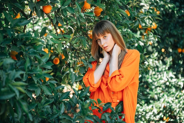 Menina bonita é vestido laranja está posando segurando as mãos atrás do pescoço para a câmera no jardim laranja