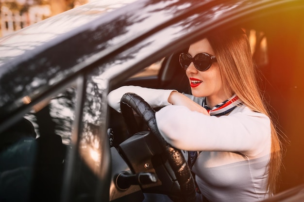 Foto menina bonita elegante em lábios vermelhos sorrindo sentado em um carro dirigindo