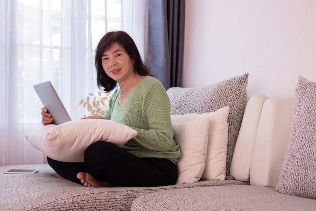 Menina bonita em casa que usa o portátil no sofá, mulher asiática idosa.