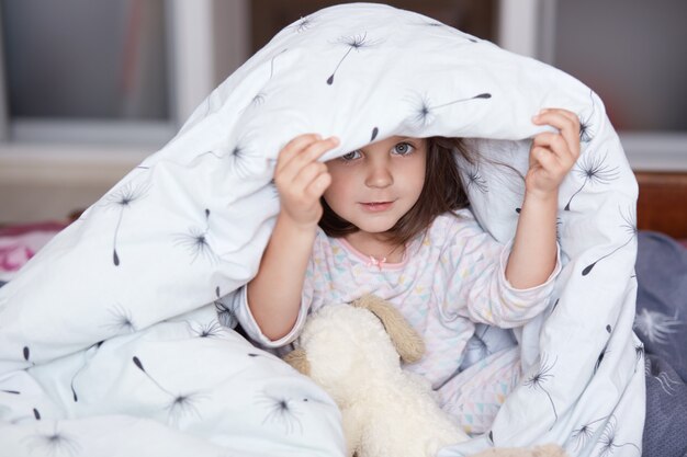 Menina bonita em roupa de noite sentado sob o cobertor com dente de leão