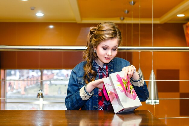 Foto menina bonita em um café olhando no saco do presente