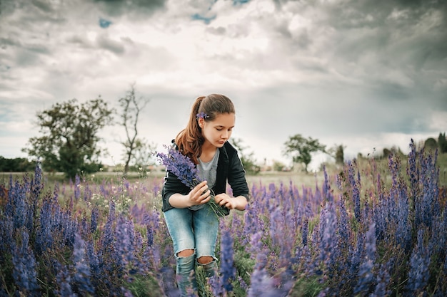 Menina bonita em um campo de primavera coleta flores roxas.