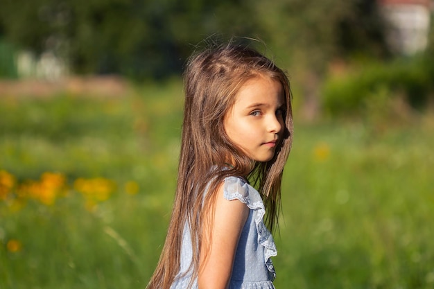 Foto menina bonita em um vestido azul com os pés descalços no verão na rua em um fundo verde