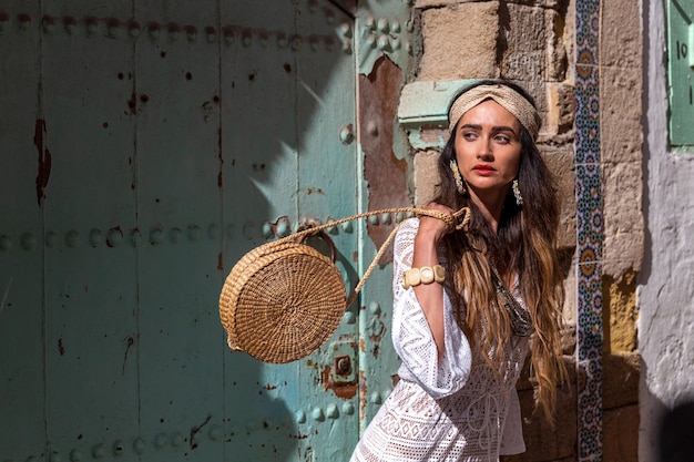 Menina bonita em um vestido branco perto da porta verde marroquina. Essaouira. Marrocos