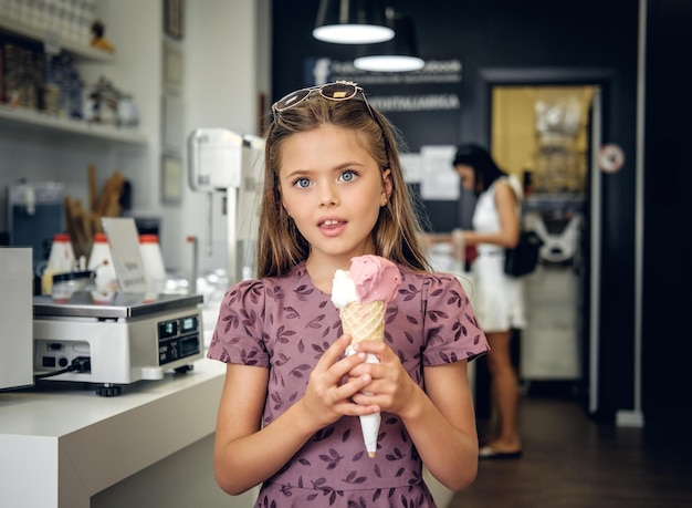 Menina bonita em um vestido, comendo sorvete em um café.