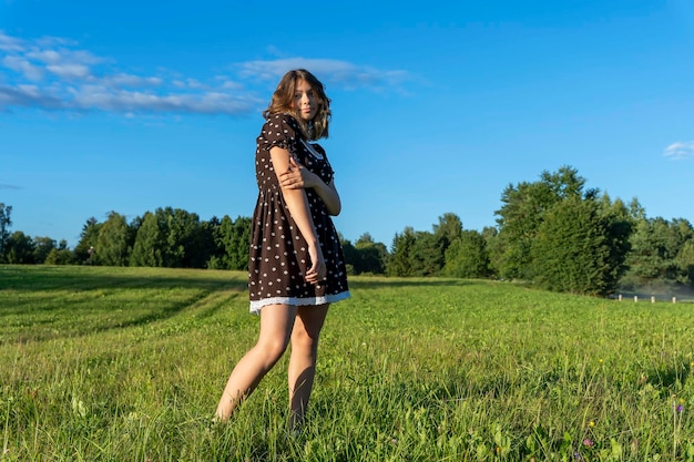 Menina bonita em um vestido curto no fundo de um campo verde no verão no sol poente