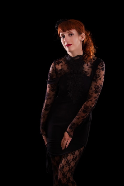 Menina bonita em um vestido gótico preto com o cabelo vermelho isolado em um fundo preto.
