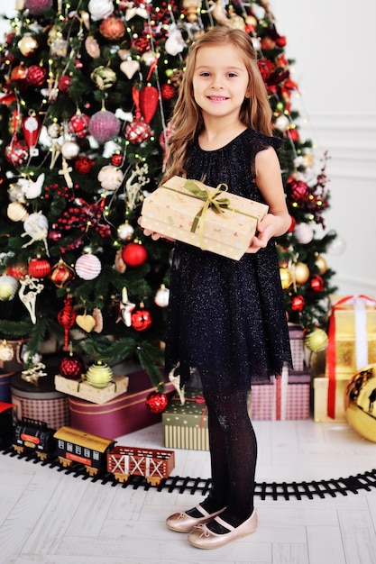 Menina bonita em um vestido preto inteligente, segurando uma caixa com um presente e sorrindo