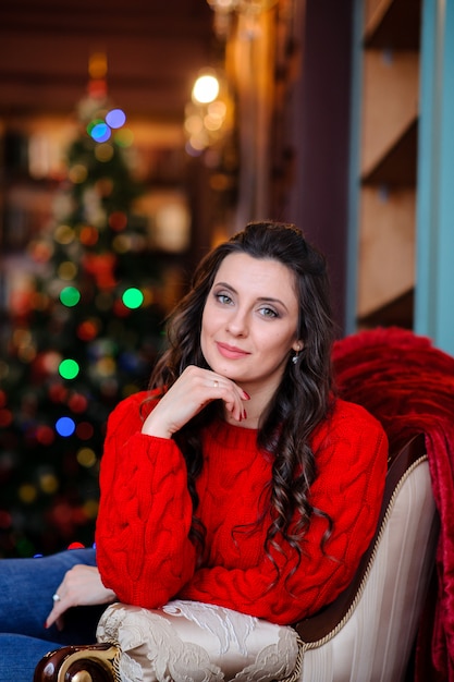 Menina bonita em uma camisola vermelha perto da árvore de Natal.