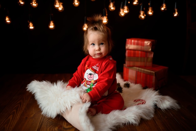 Menina bonita em uma fantasia de natal vermelha com guirlandas retrô senta-se em uma pele