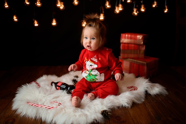 Menina bonita em uma fantasia de Natal vermelha com guirlandas retrô senta-se em uma pele