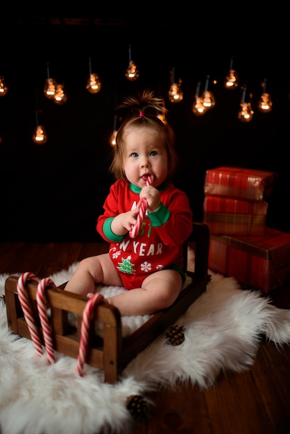 Menina bonita em uma fantasia de Natal vermelha com guirlandas retrô senta-se em uma pele