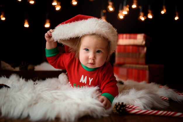 Menina bonita em uma fantasia de natal vermelha com guirlandas retrô senta-se em uma pele